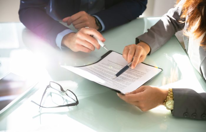 Two Businesspeople Hand Analyzing Document Over Glass Desk